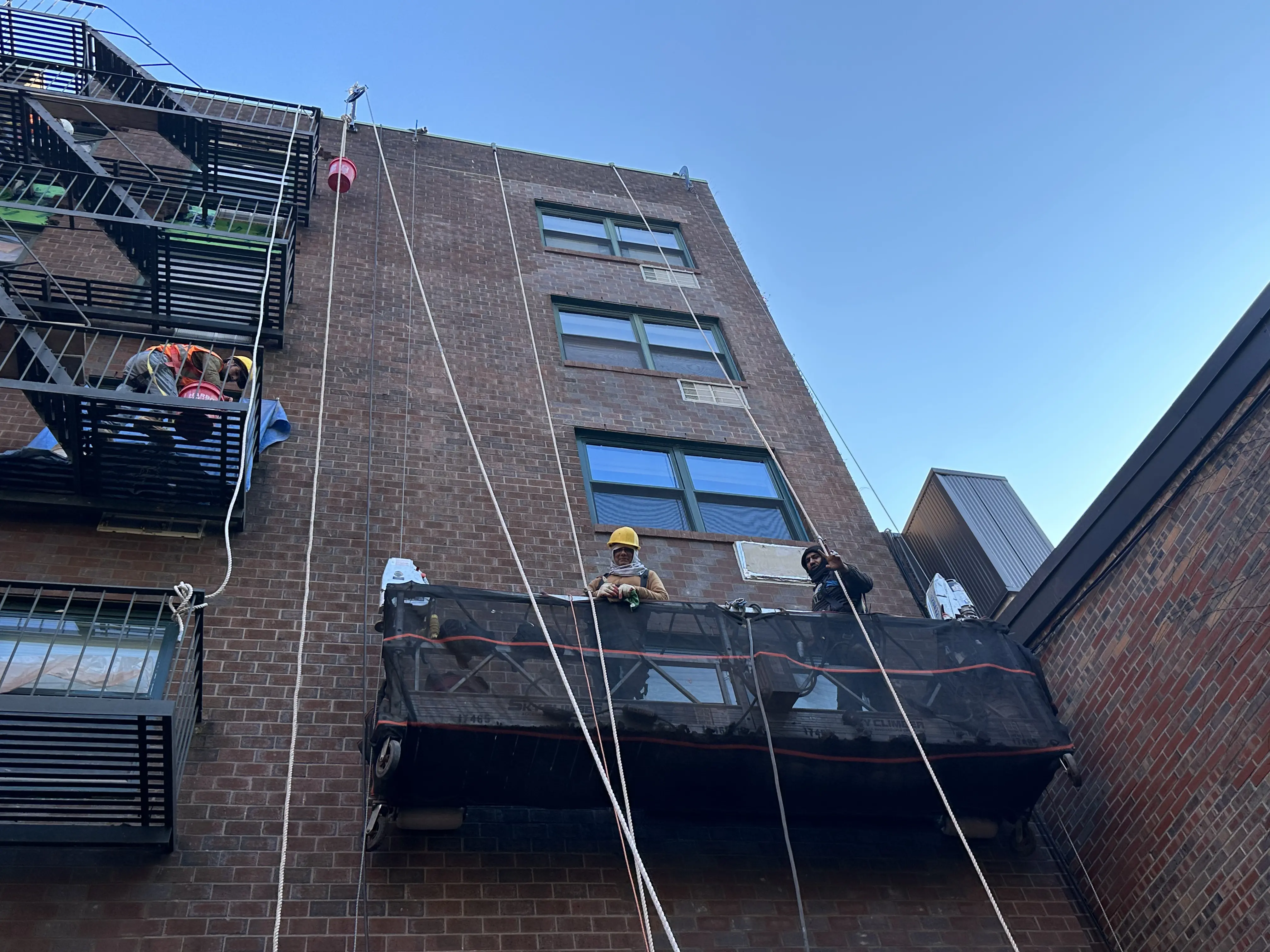 Mason Construction team restoring brick façade of NYC residential building using suspended scaffolding.